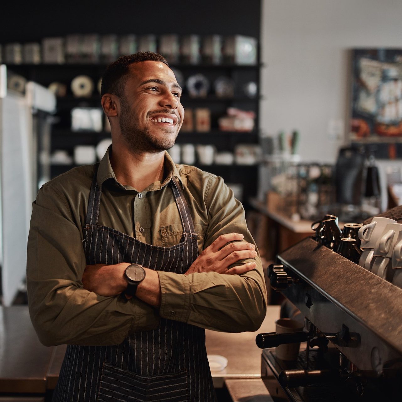 Successful handsome male cafe owner standing with arms crossed looking away thinking about future